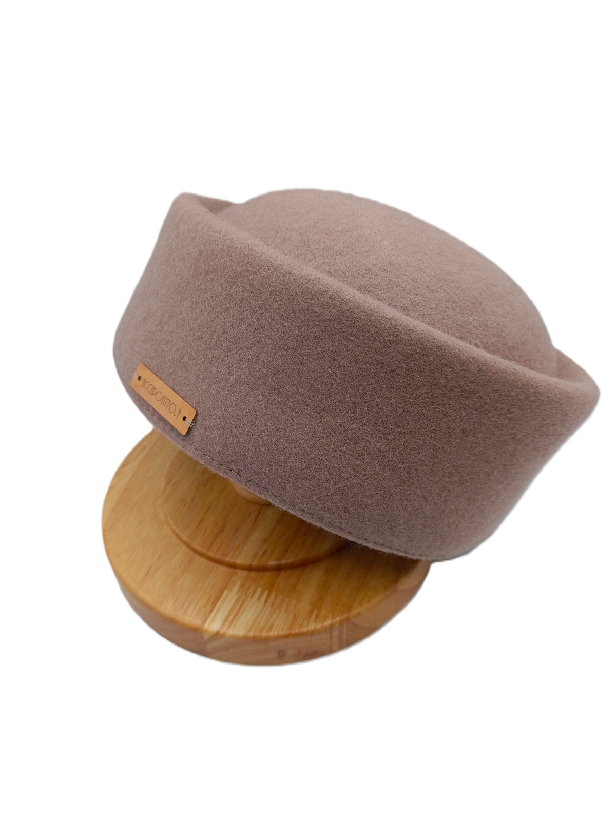 Cappello pillbox Chèrie del brand Accapofitto di feltro di lana beige con targhetta logo color rame, in posa su un sostegno di legno