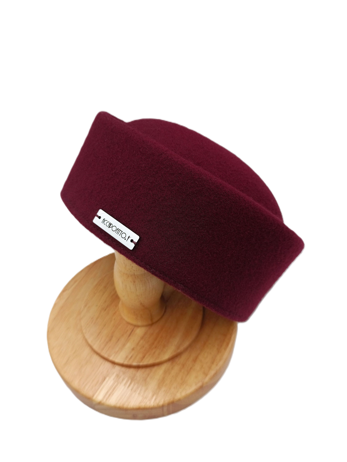 Cappello pillbox Chèrie del brand Accapofitto, in morbido feltro di lana color bordeaux e targhetta con logo, appoggiato su supporto di legno
