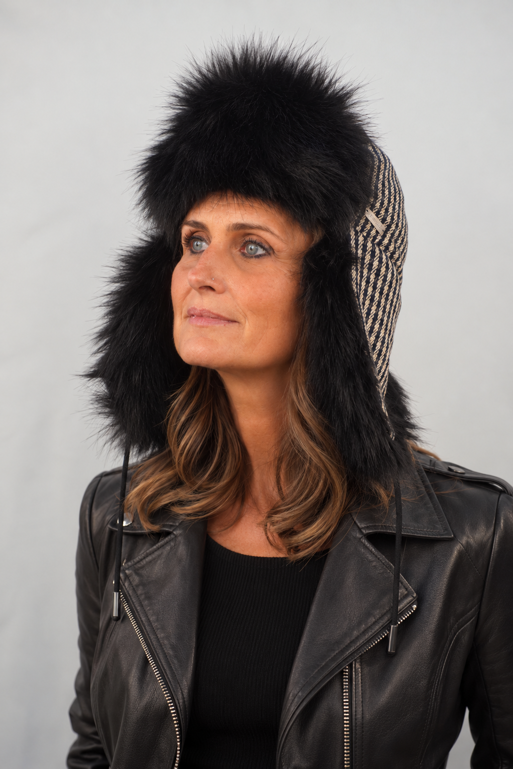Cappello aviatore Mika del brand Accapofitto. Tessuto esterno a quadretti blu e avorio stile pied de poulet, rifinito con ecopelliccia variante nera. Indossato da una modella