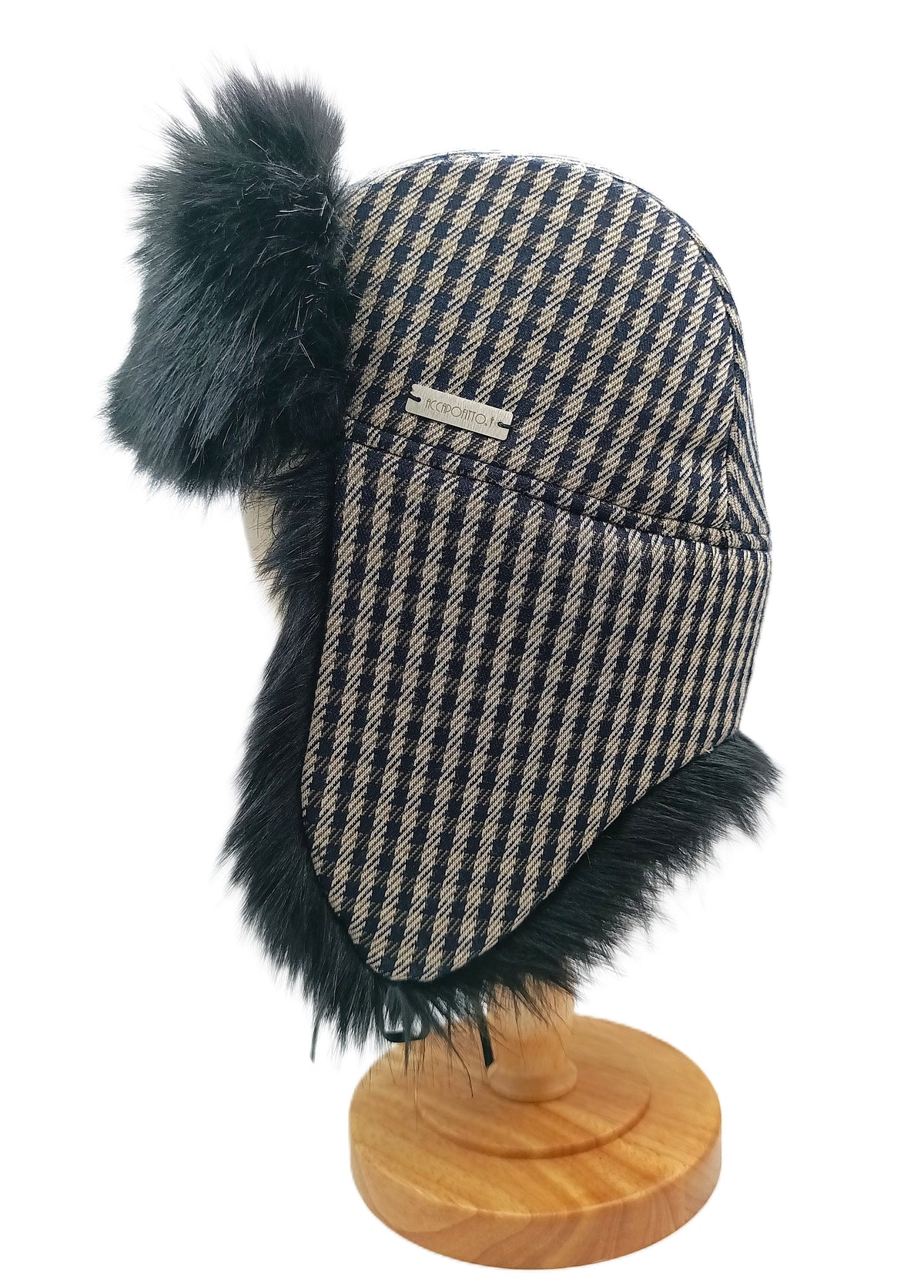 Cappello aviatore Mika del brand Accapofitto. Tessuto esterno a quadretti blu e avorio stile pied de poulet, rifinito con ecopelliccia variante nera. Su sostegno di legno