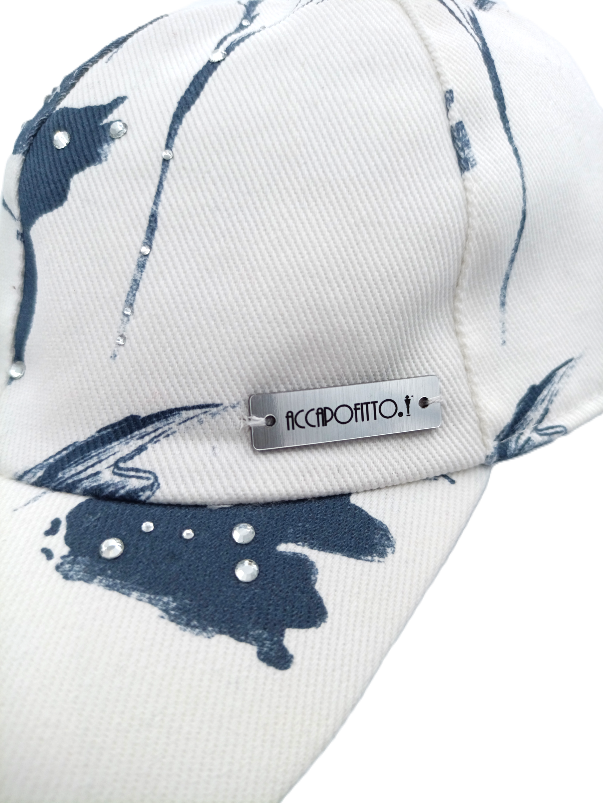 Cappello baseball del brand Accapofitto, in cotone bianco e disegno floreali blu, con strass. Dettaglio sull'etichetta