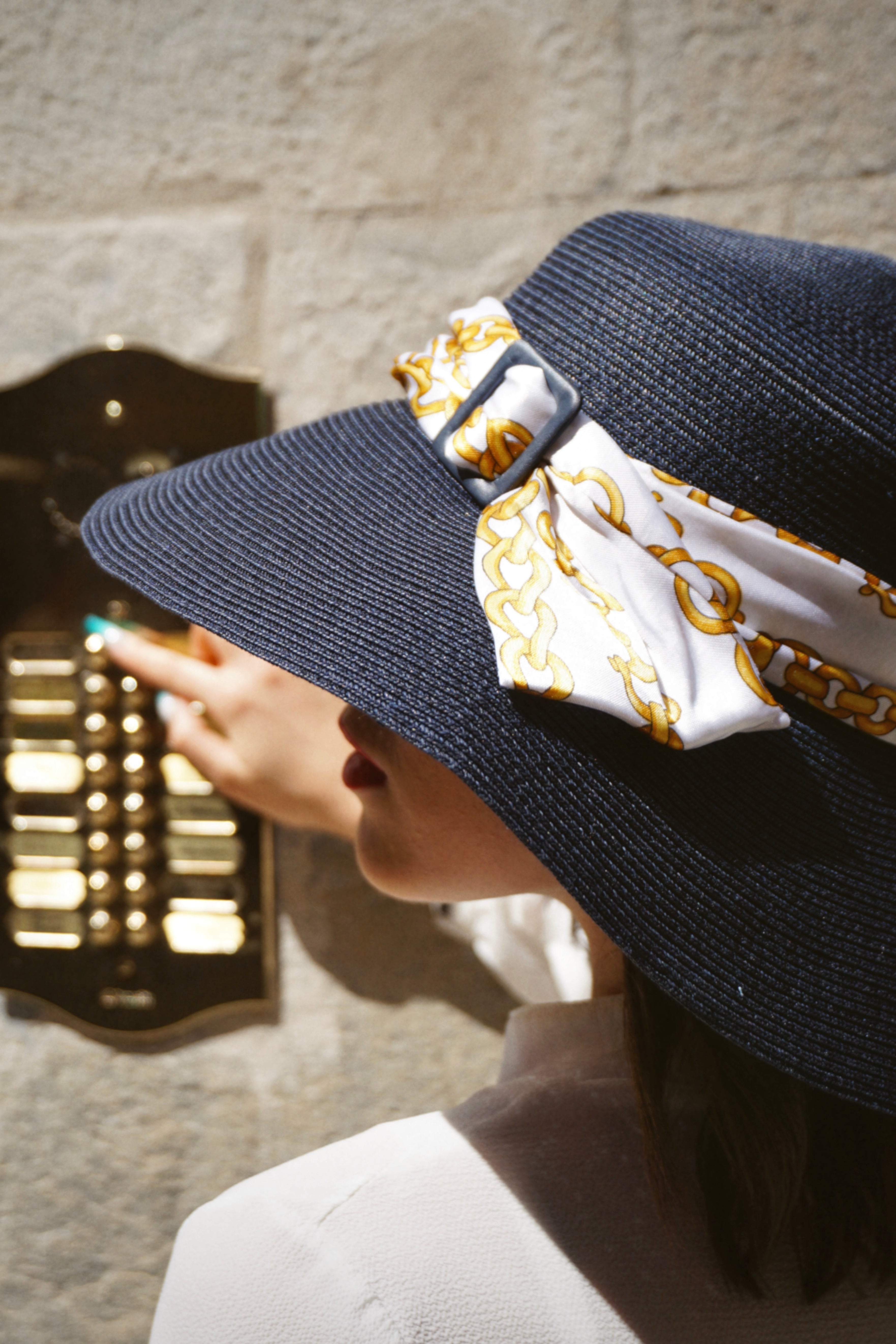 Cappello elegante di carta colore blu, decorato con foulard bianco e disegni oro, con fibbia blu, indossato da una modella
