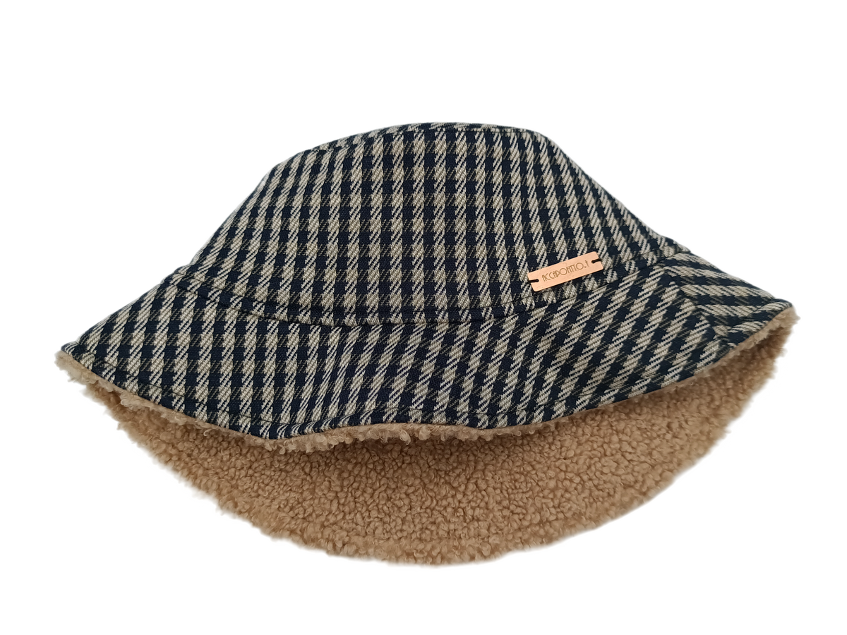 Cappello bucket hat Mabel del brand Accapofitto, realizzato con tessuto a quadretti blu e beige all'esterno e con tessuto teddy color cammello all'interno
