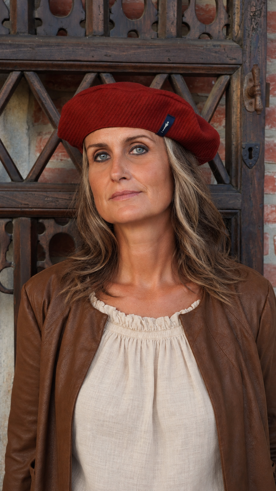 Una modella indossa il basco Amelie del brand Accapofitto. Il basco è di lana vergine color mattone e la modella è vestita con giubbotto di pelle marrone e camicia beige