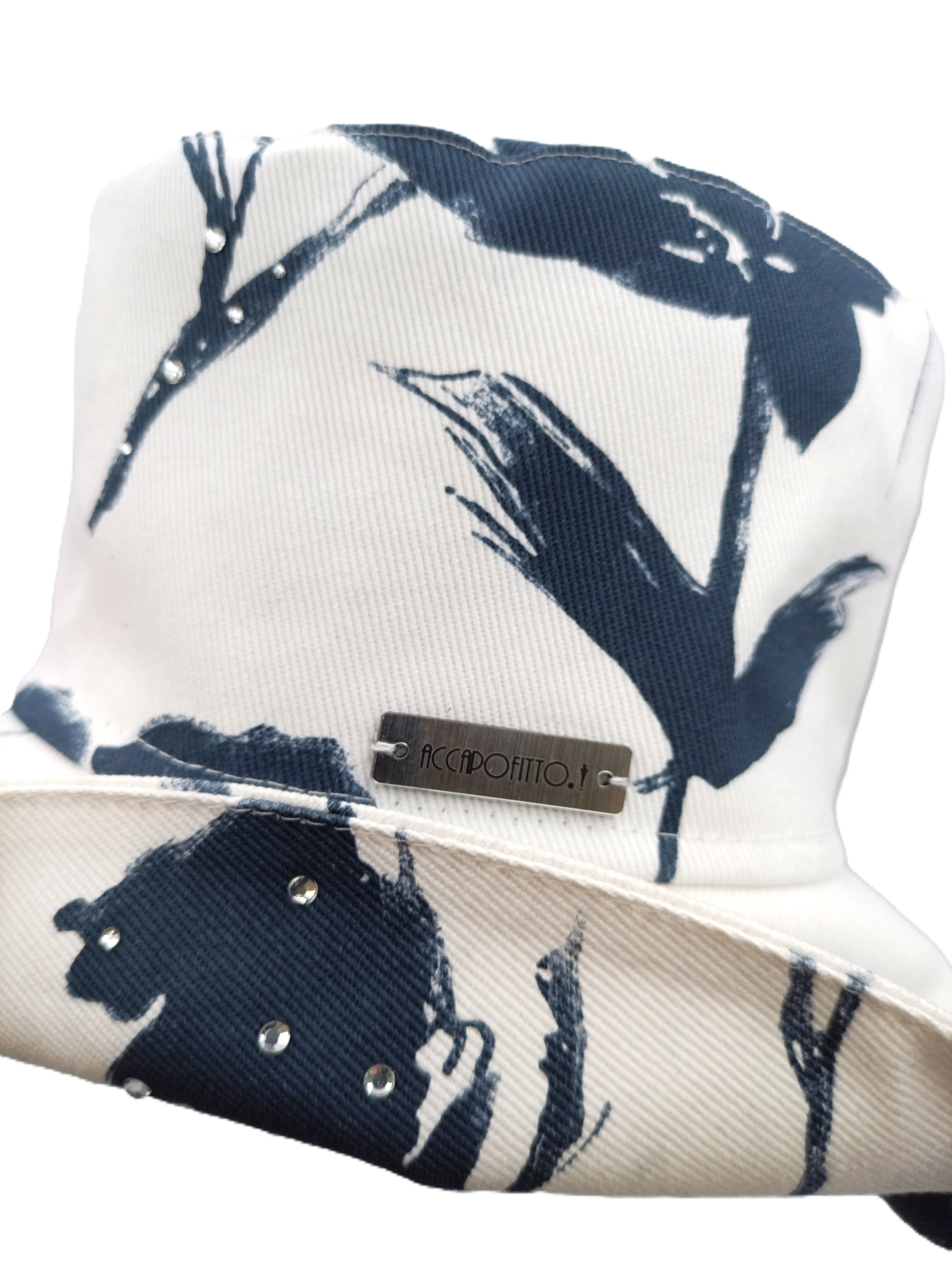 Cappello bucket hat del brand Accapofitto. Cotone bianco con fantasia a fiori blu, impreziosito da piccoli strass. dettaglio sull'etichetta
