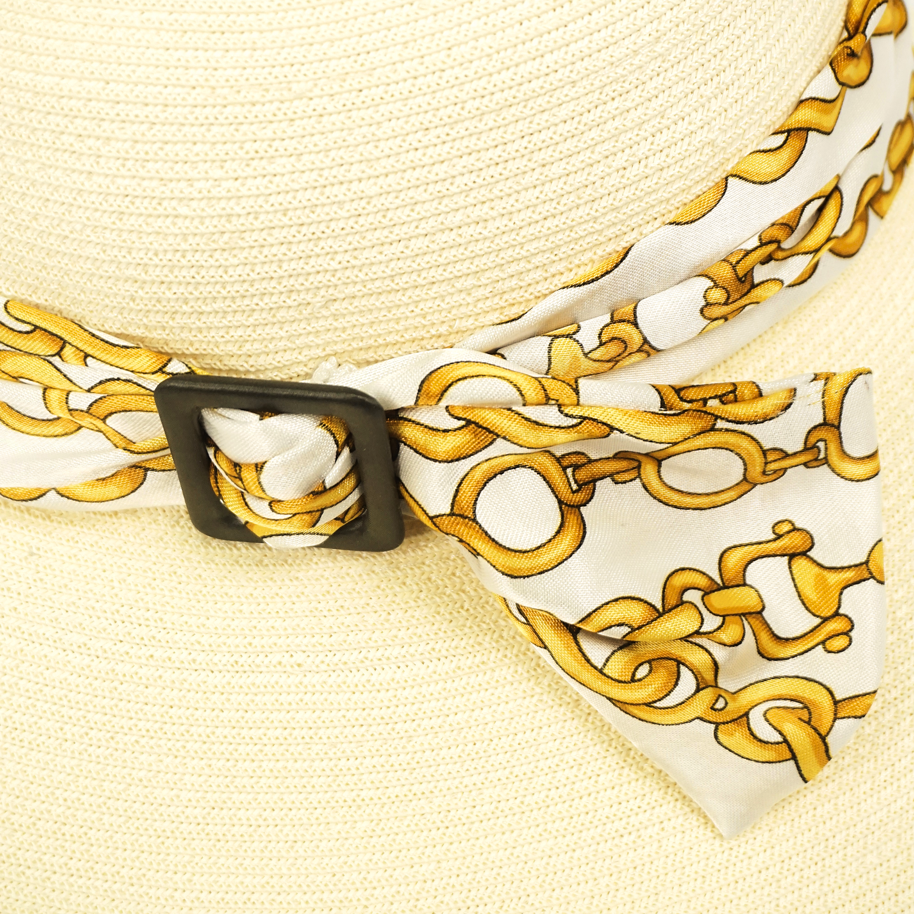 Cappello di carta del brand Accapofitto, color panna, con nastro di viscosa bianco e disegni dorati, con fibbia similpelle nera. Particolare.