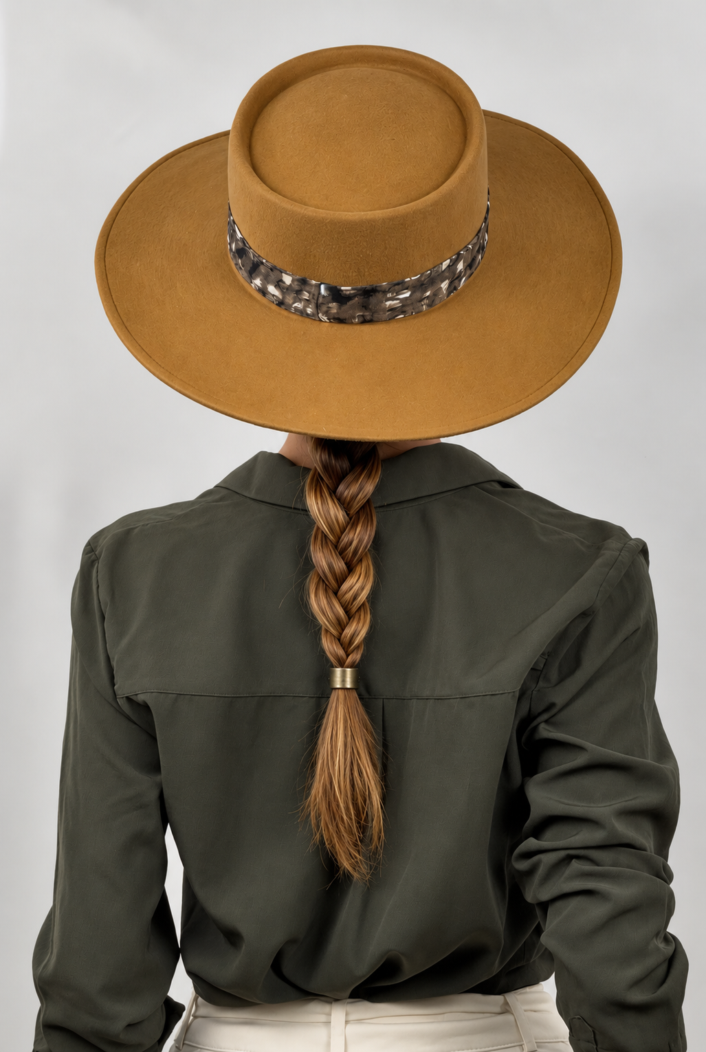 Una modella indossa il cappello di feltro color cammello Jane del brand Accapofitto, impreziosito da una fascia maculata sui toni del verde, nero e panna, con etichetta logo color rame. Visione dal retro