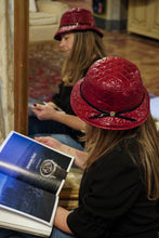 Carica l&#39;immagine nel visualizzatore di Gallery, La cloche Nathalie di Accapofitto in tessuto trapunato rosso indossato da una donna che legge una rivista di moda
